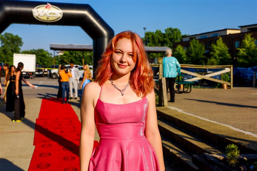 A young woman wearing a pink dress stands on the red carpet
